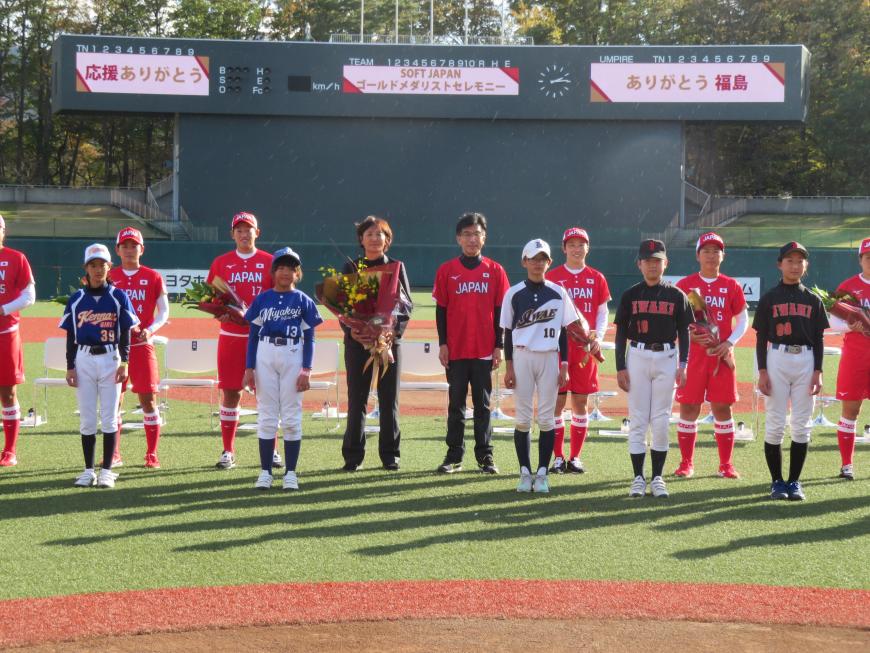 球場で花束を持って整列しているユニフォーム姿の日本代表選手と市長の前に、ユニフォームを着た少年少女の選手たちが並んで立っている写真