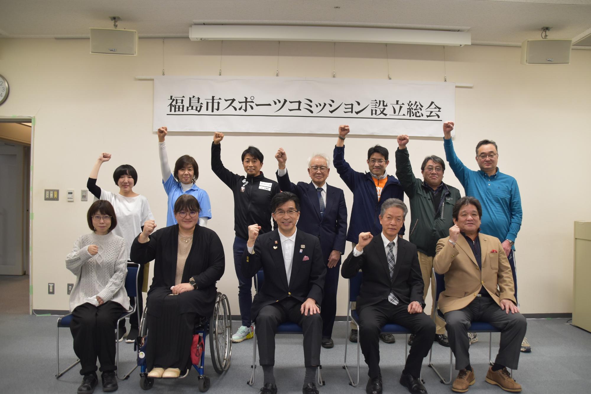 「福島市スポーツコミッション設立総会」の吊りパネル前で、市長と関係者が2列に並び、握りこぶしでポーズを取っている写真