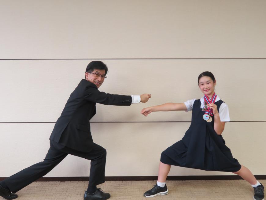 市長と制服姿の女子児童がお互いにフェンシングの付きのポーズをしている写真