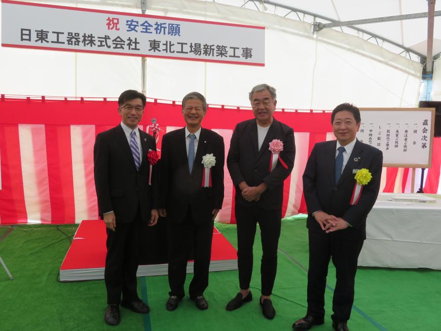 「日東工器株式会社東北工場新築工事」のボードが吊るされたテント内で、胸章をつけた市長と隈研吾さんを含む男性4名が並んで撮影した写真