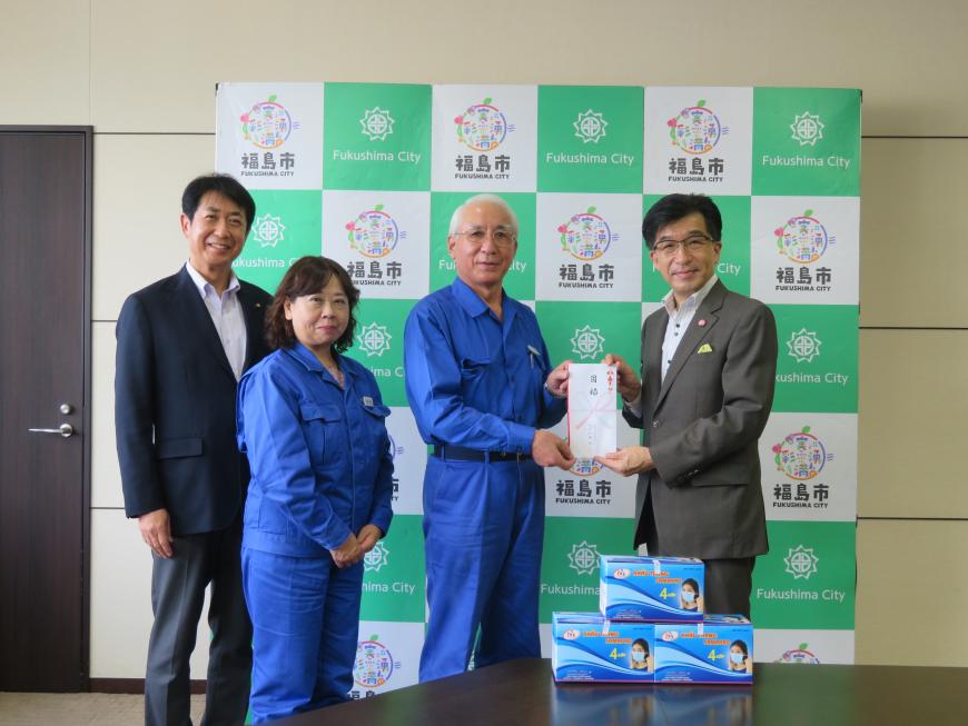 バックパネルの前で、市長と男性で目録封筒を持ち、横に男性と女性が立っている写真
