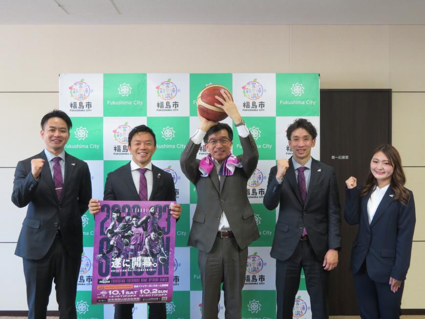 男性3名、女性1名の真ん中にバスケットボールを掲げた市長が立ち、試合のポスターを持っている男性以外はガッツポーズをしている写真