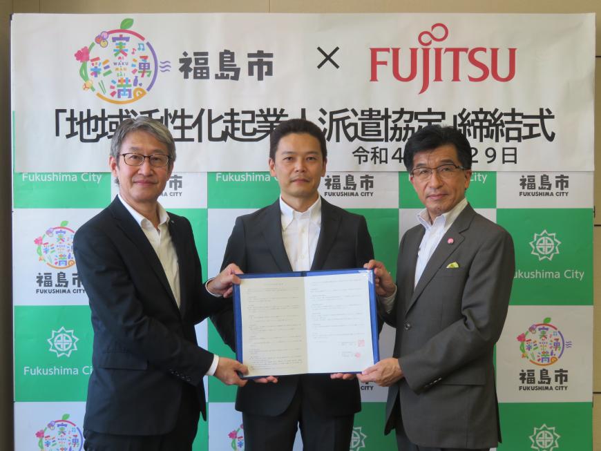 バックパネルの前で、市長と男性2名で協定書ファイルを広げて持っている写真
