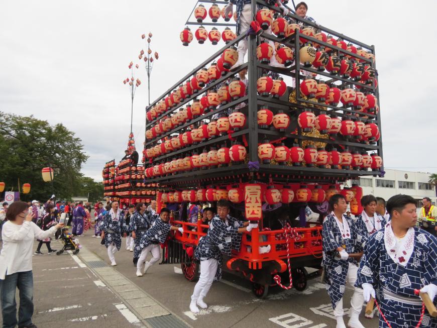沿道の方が見ている中、提灯が飾られた山車を大勢の人で引っ張っている写真