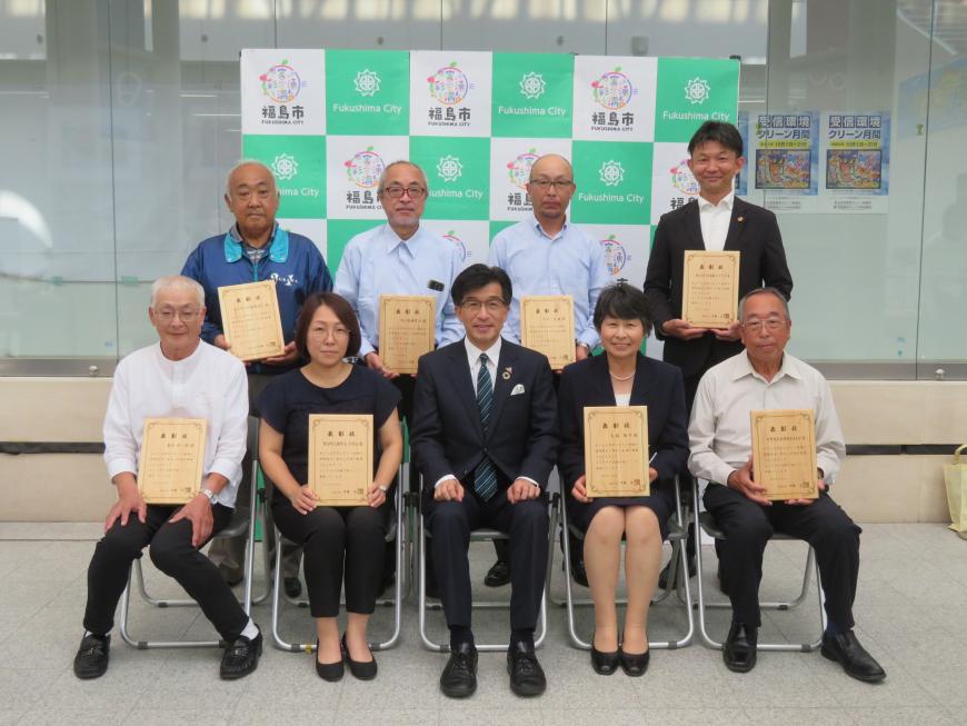 前列に市長を中心に男女各2名が座り、後列に男性4名が立ち、それぞれ賞状を持っている集合写真
