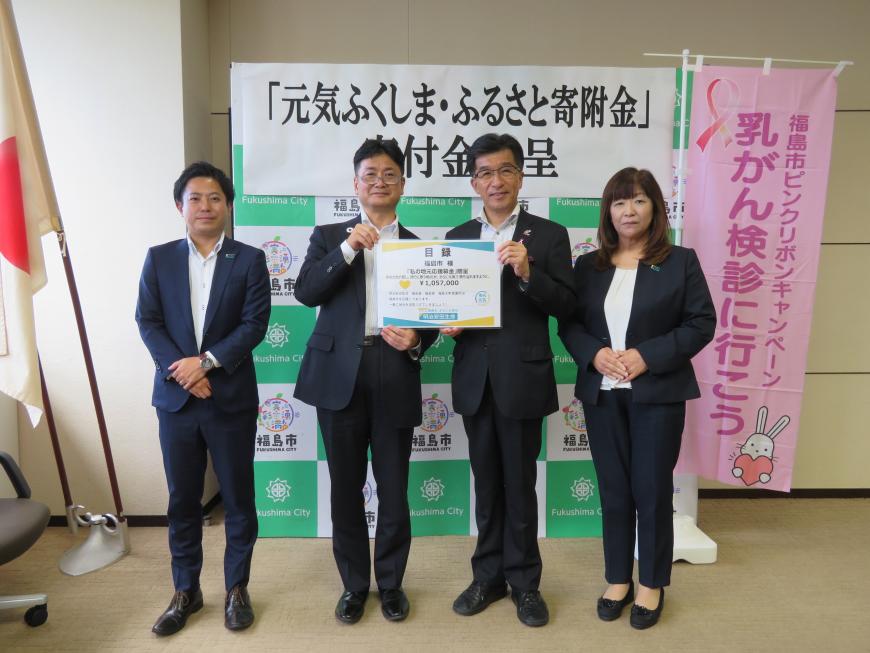 「乳がん検診に行こう」の幟があるバックパネルの前に市長を含めて男性3名と女性1名が立ち 目録を市長と男性で持っている写真
