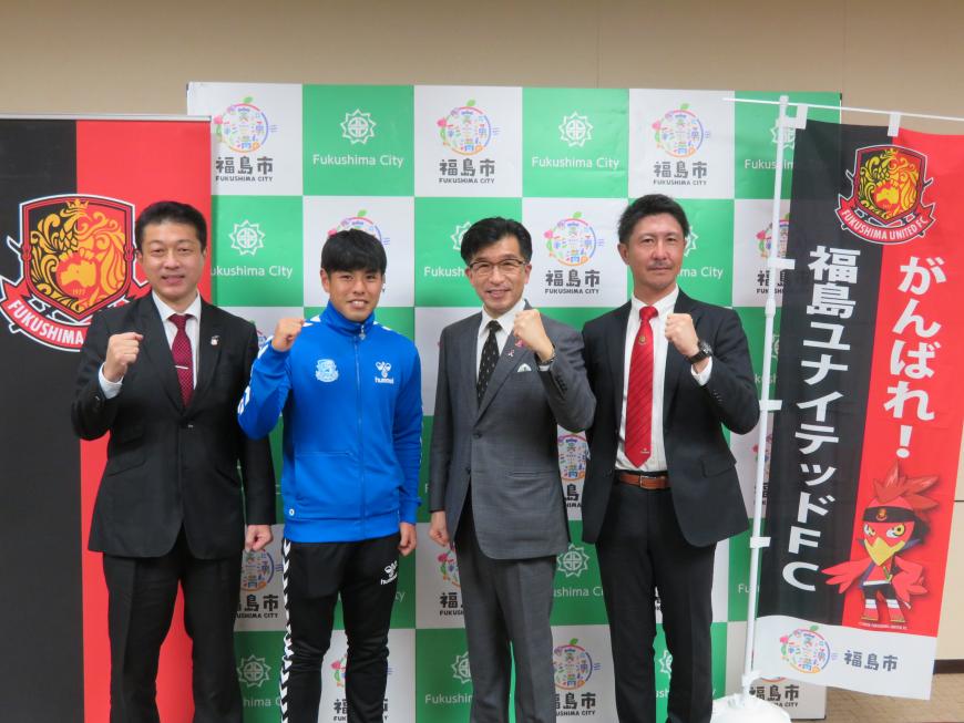 バックパネルの前に「がんばれ福島ユナイテッドFC」と書かれたのぼりが置いてある横で市長とジャージ姿の選手とスーツを着た男性2人がガッツポーズをしている写真