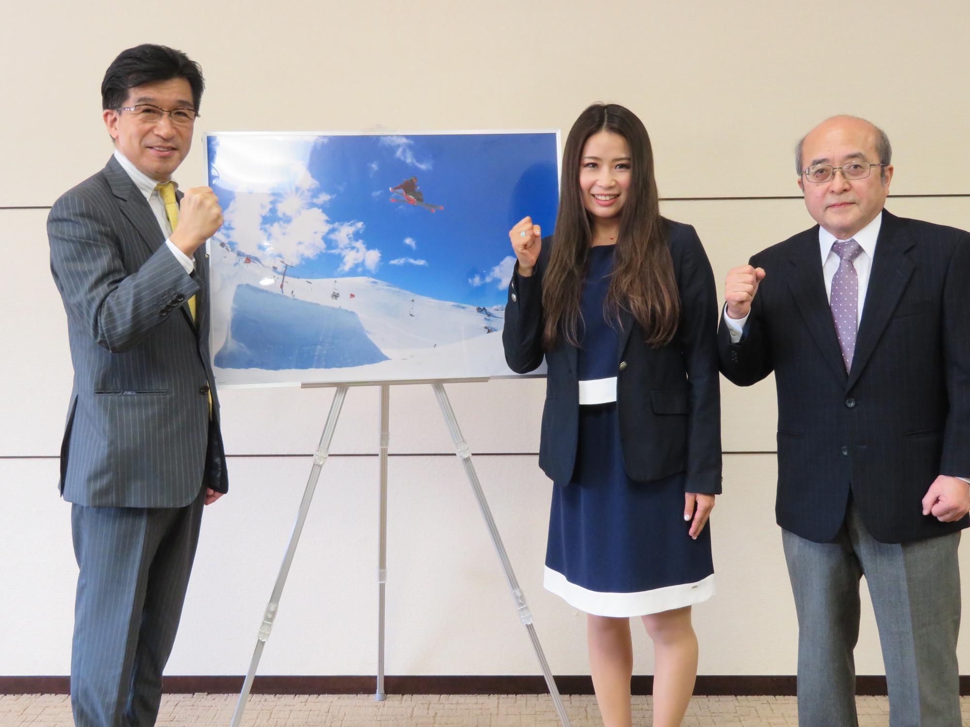 写真の前で、市長と佐藤瞳さんと関係者が握りこぶしでポーズを取っている写真
