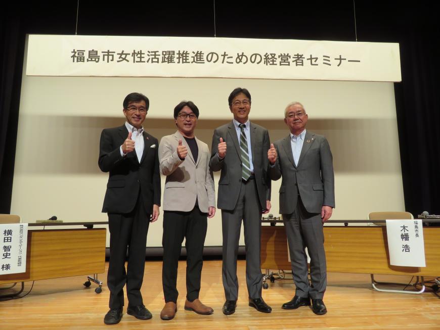 「福島市女性活躍推進のための経営者セミナー」の横断幕があるステージで市長を含む男性4名が親指を立てたポーズをしている写真
