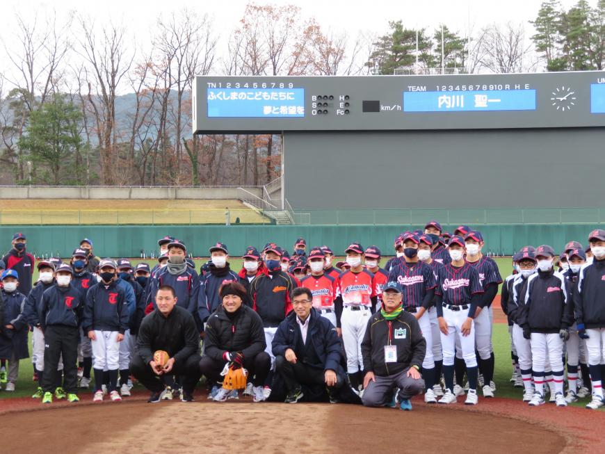 球場のマウンド付近に内川選手と市長、他男性2人が腰を下ろした姿勢で、その後ろに野球教室に参加した子どもたちがチーム毎に整列して立っている集合写真