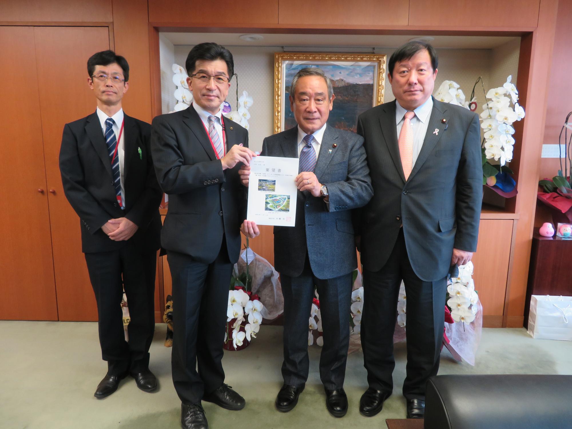 二人の男性の間に立った市長と大西英男国土交通副大臣が要望書を手に持っている写真