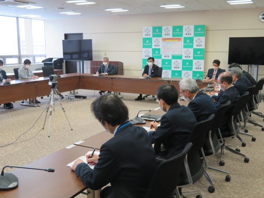 四角に配置された机に座っている職員に対して、中央に座っている市長が話をしている写真