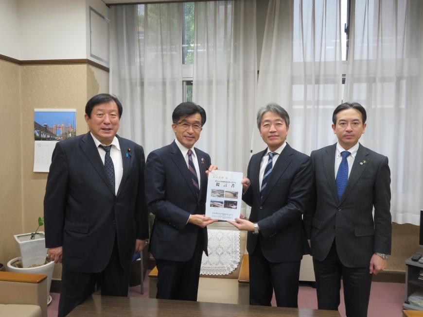 執務室内で市長と男性で要望書を持ち、その両脇に男性各1名立っている写真