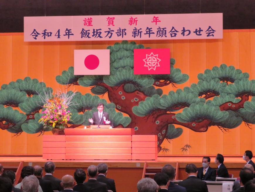 舞台幕に松の木が描かれたステージで、座っている参加者の前で、市長が演台に立って話をしている写真