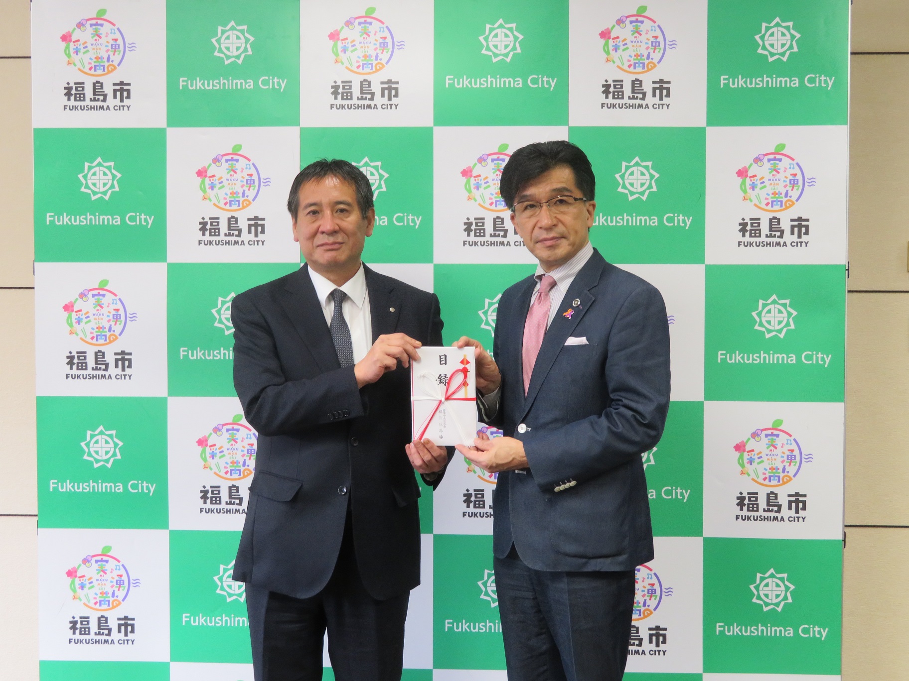 福島市のバックパネル前で、日本中央競馬会の関係者と市長が目録の封筒を持っている記念写真