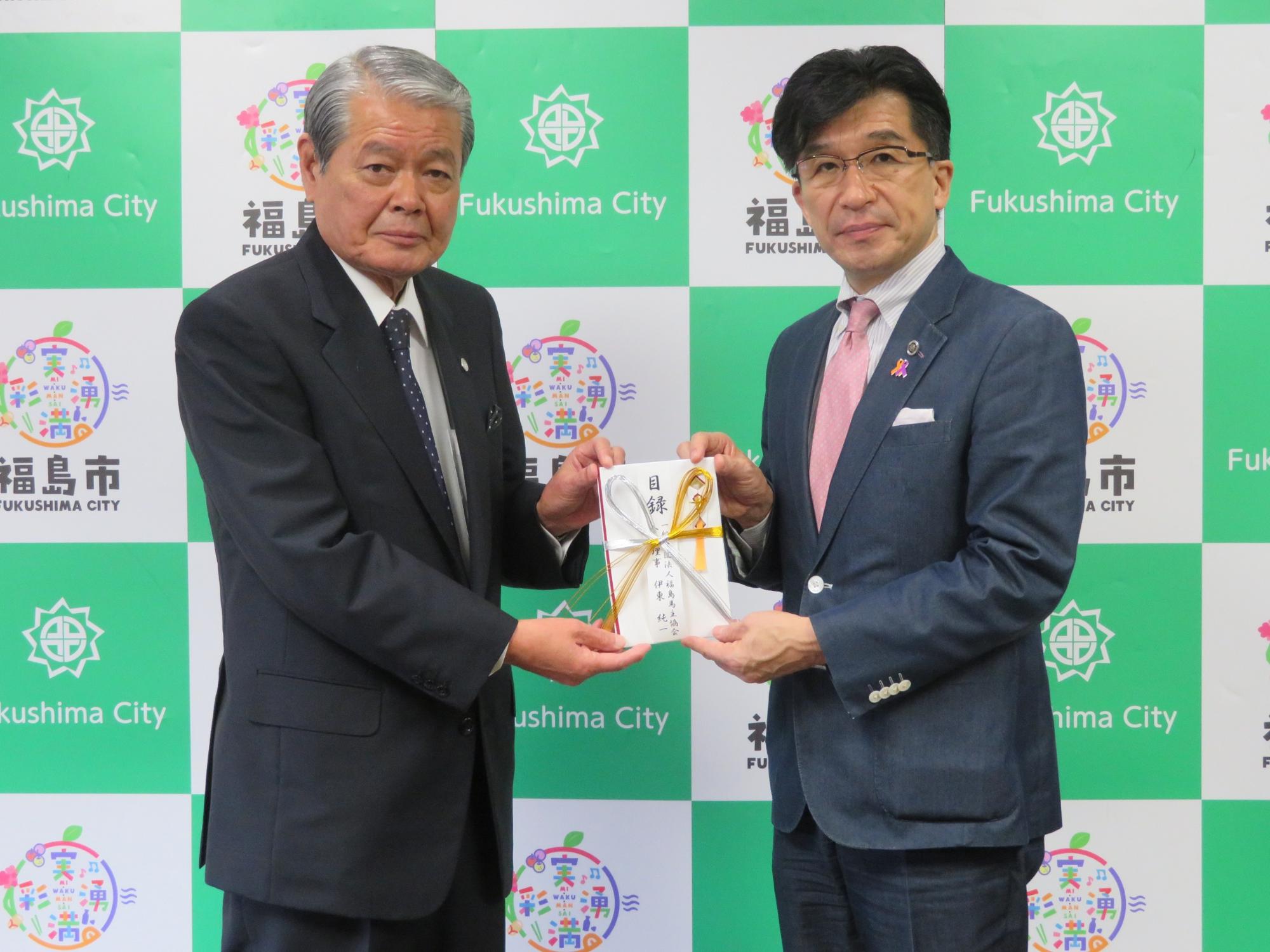 福島市のバックパネル前で、福島馬主協会の関係者と市長が目録の封筒を持っている記念写真