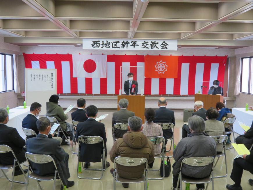 「西地区新年交歓会」と書かれた横断幕の下に紅白幕が貼られた会場で、座っている参加者の前で、市長が演台に立って話をしている写真