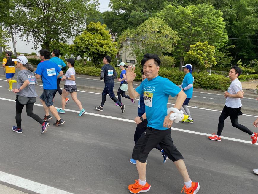 青のTシャツを着て走っている市長が沿道に向けて手を挙げている写真