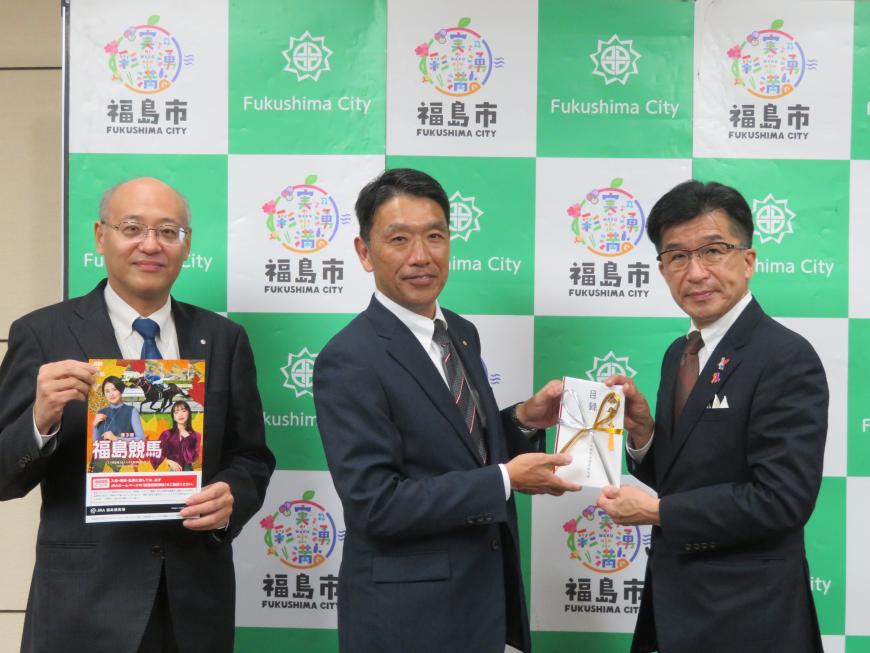 バックパネルの前で、市長と男性で目録を持ち、その横で男性が福島競馬のパンフレットを持っている写真