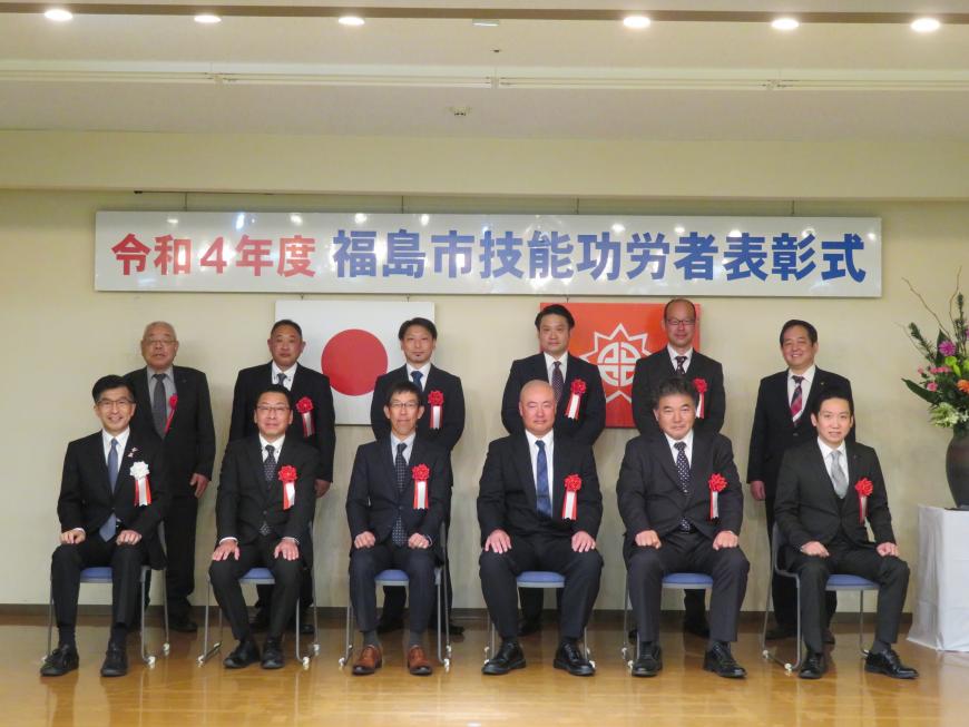 「令和4年度 福島市技能功労者表彰式」と書かれたボードがある会場で、表彰された9名が市長と一緒に2列に並んでいる記念写真