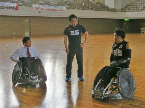 競技用車いすに乗った市長と選手がユニフォームを着て中央に立った男性を見ている写真
