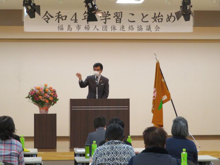 「学習こと始め」と書かれた横断幕がある会場で、座っている参加者の前で、市長が一段高くなったステージの演台に立って話をしている写真