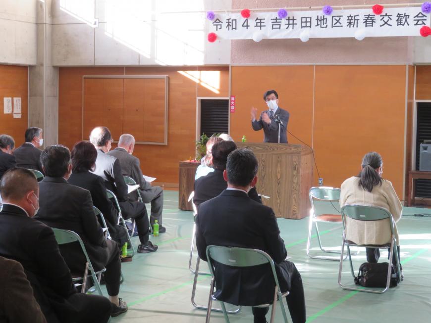 吉井田地区新春交歓会の横断幕がある会場で、座っている参加者の前で、市長が演台に立って話をしている写真