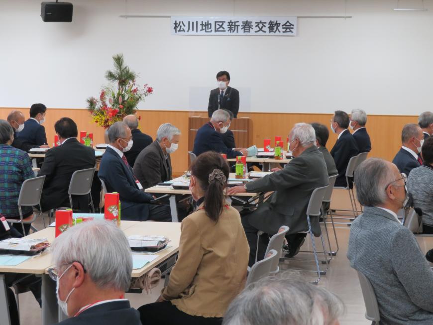 「松川地区新春交歓会」の横断幕がある会場で、座っている参加者の前で、市長が演台に立って話をしている写真