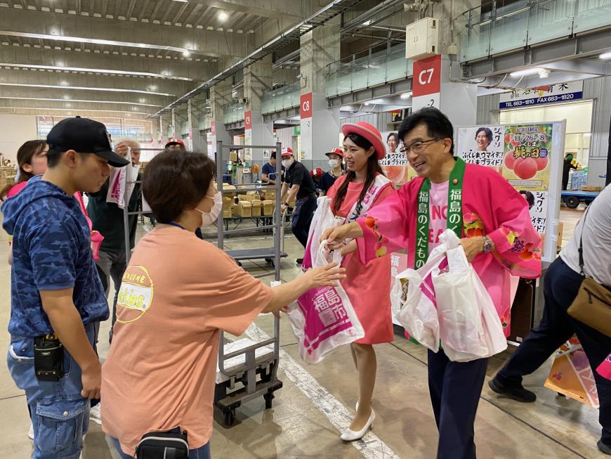 市場内で法被を着た市長とミスピーチガールが来場された方にビニール袋を渡している写真