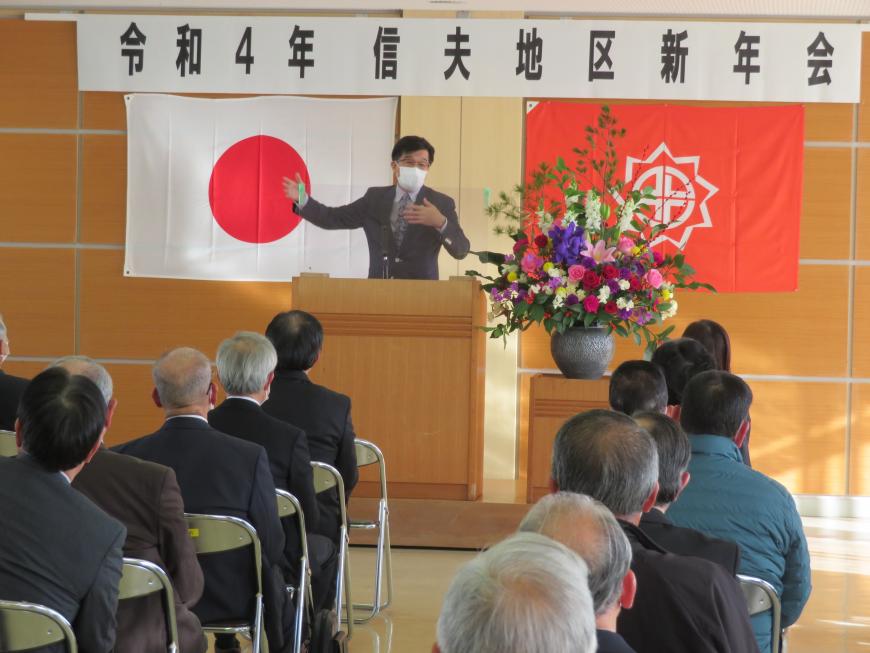 信夫新年会の横断幕がある会場で、座っている参加者の前で、市長が演台に立って話をしている写真
