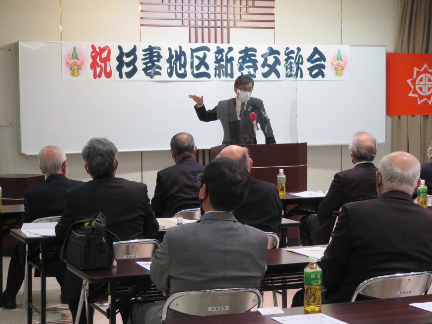「杉妻地区新春交歓会」の横断幕がある会場で、座っている参加者の前で、市長が演台に立って話をしている写真