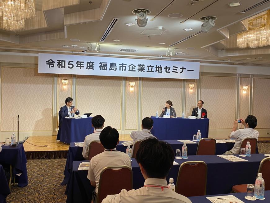 「令和5年度福島市企業立地セミナー」と書かれた横断幕が書かれたステージに市長と2名のパネラーが座り話をしているところを、参加者が聞いている写真