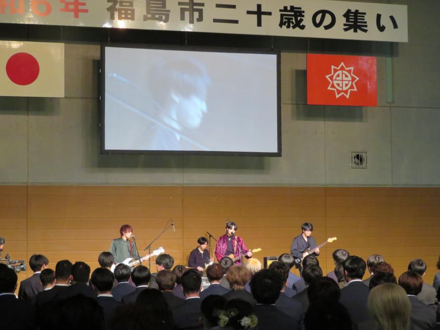 多くの参加者が見ている中、ステージで4人組のバンドが演奏している写真