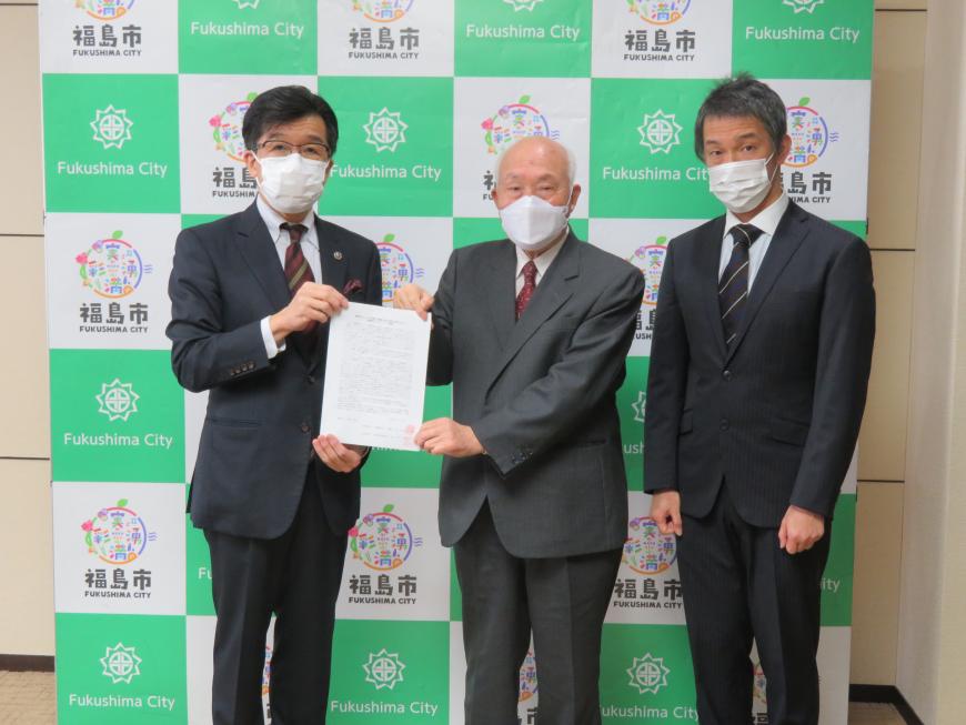 バックパネルの前で、市長と男性で要望書を持ち、横に男性が並んでいる写真