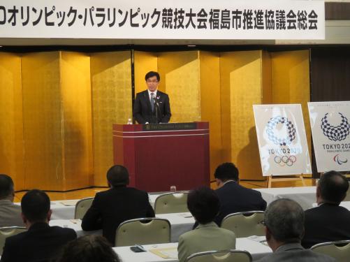 「オリンピック・パラリンピック競技大会福島市推進協議会総会」の看板が掲げられた舞台の金屏風の前の演台に立つ市長が話をしている写真
