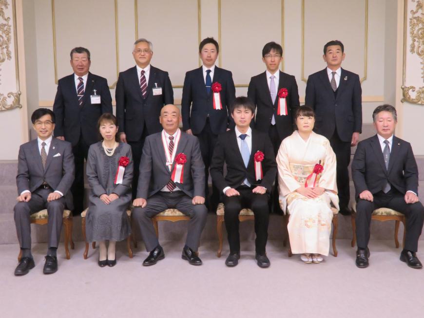 前列に市長と胸章をつけた男性2人、女性2人が座り、後列に胸章をつけた男性2人と他男性3人が立っている写真