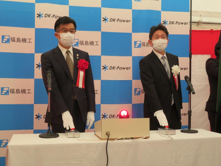 バックパネルの前で、市長と男性が各自の前に置かれたスイッチを押した写真