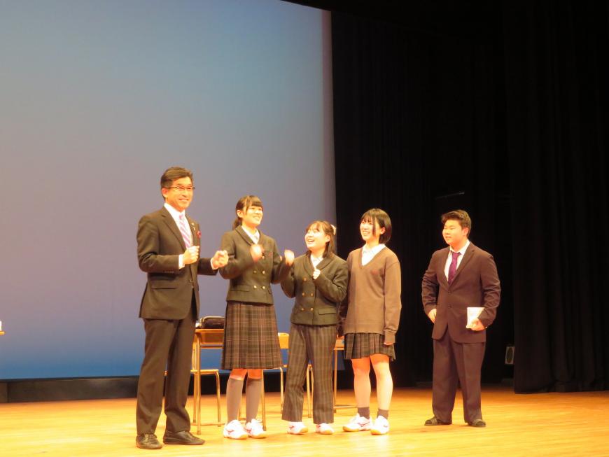 女子生徒3名、男子生徒1名が横一列に並んでいるステージに市長も参加している写真