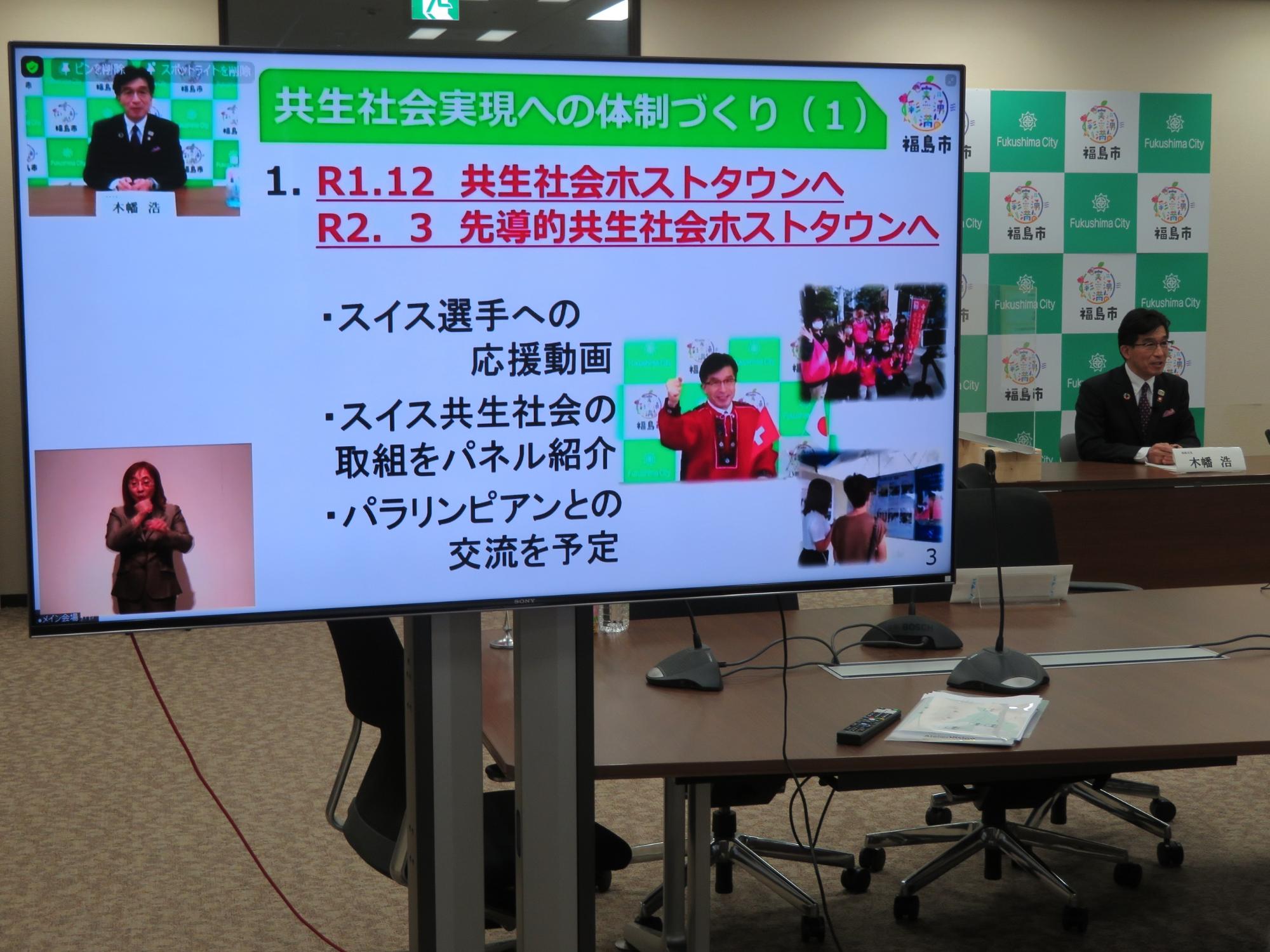 テレビモニターに「共生社会実現への体制づくり」と題した写真や資料が映し出されている写真
