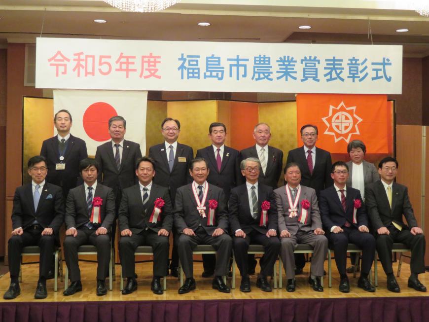 「令和5年度福島市農業賞表彰式」の横断幕がある金屛風の前で、前列に胸章をつけた男性が6名座り、後方に6名立っている記念写真