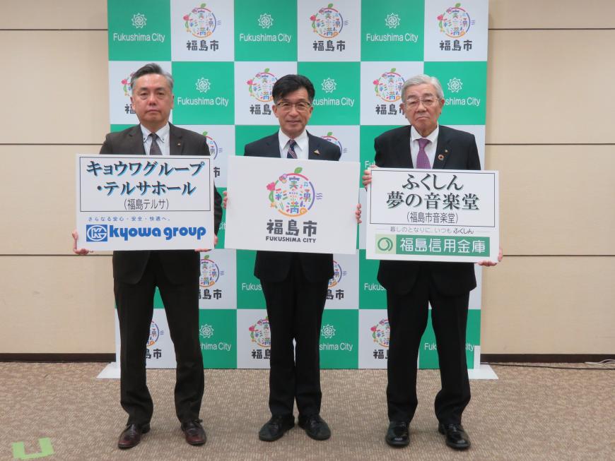 バックパネルの前で、市長が福島市のボード、右隣の男性がキョウワグループ・テルサホールのボード、左隣の男性がふくしん夢の音楽堂のボードを持ち横一列に並んでいる写真