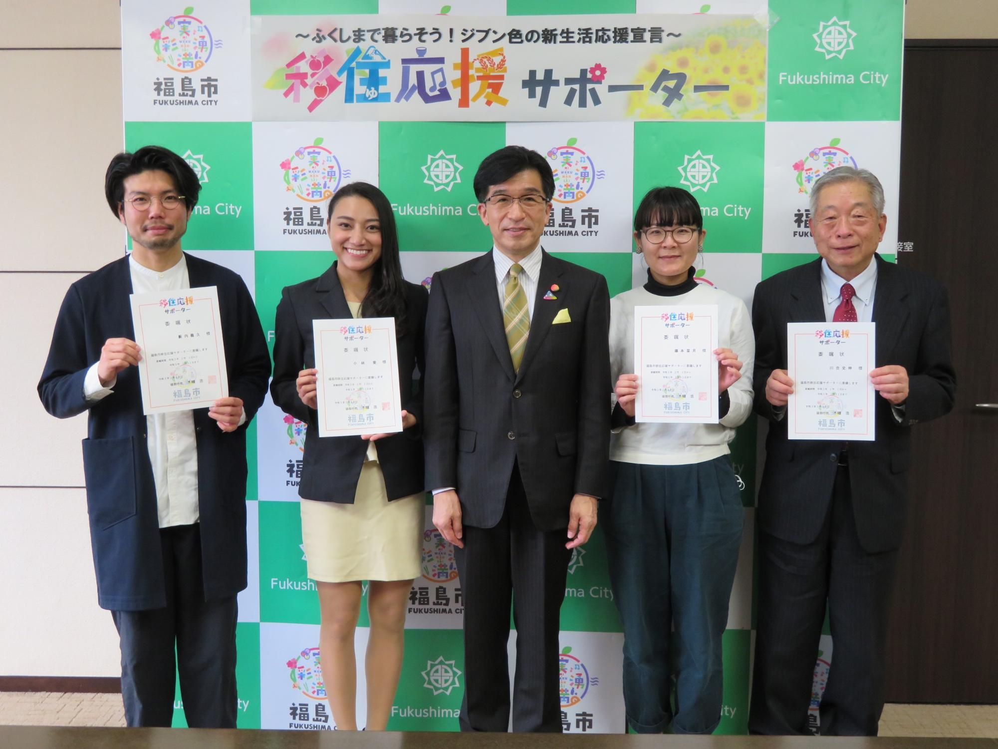 福島市のバックパネルに「移住応援サポーター」と書かれた横断幕があり、市長と交付書を手に持った関係者4名が並んでいる写真