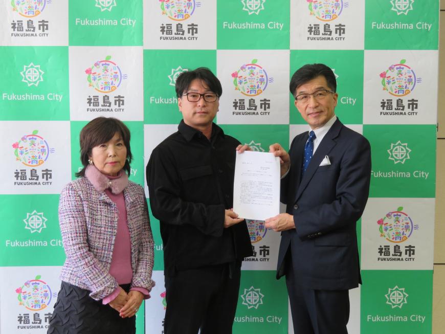 バックパネルの前に立っている男女の男性と市長で答申書を持っている写真