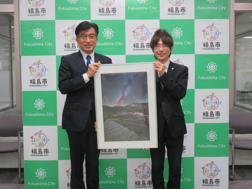 バックパネルの前で、市長と男性で額に入った写真を持っている写真