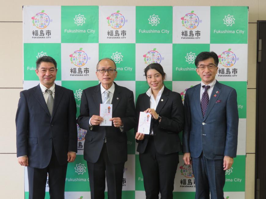 バックパネルの前で、市長と男性の間に目録を持った男性と女性が立っている写真