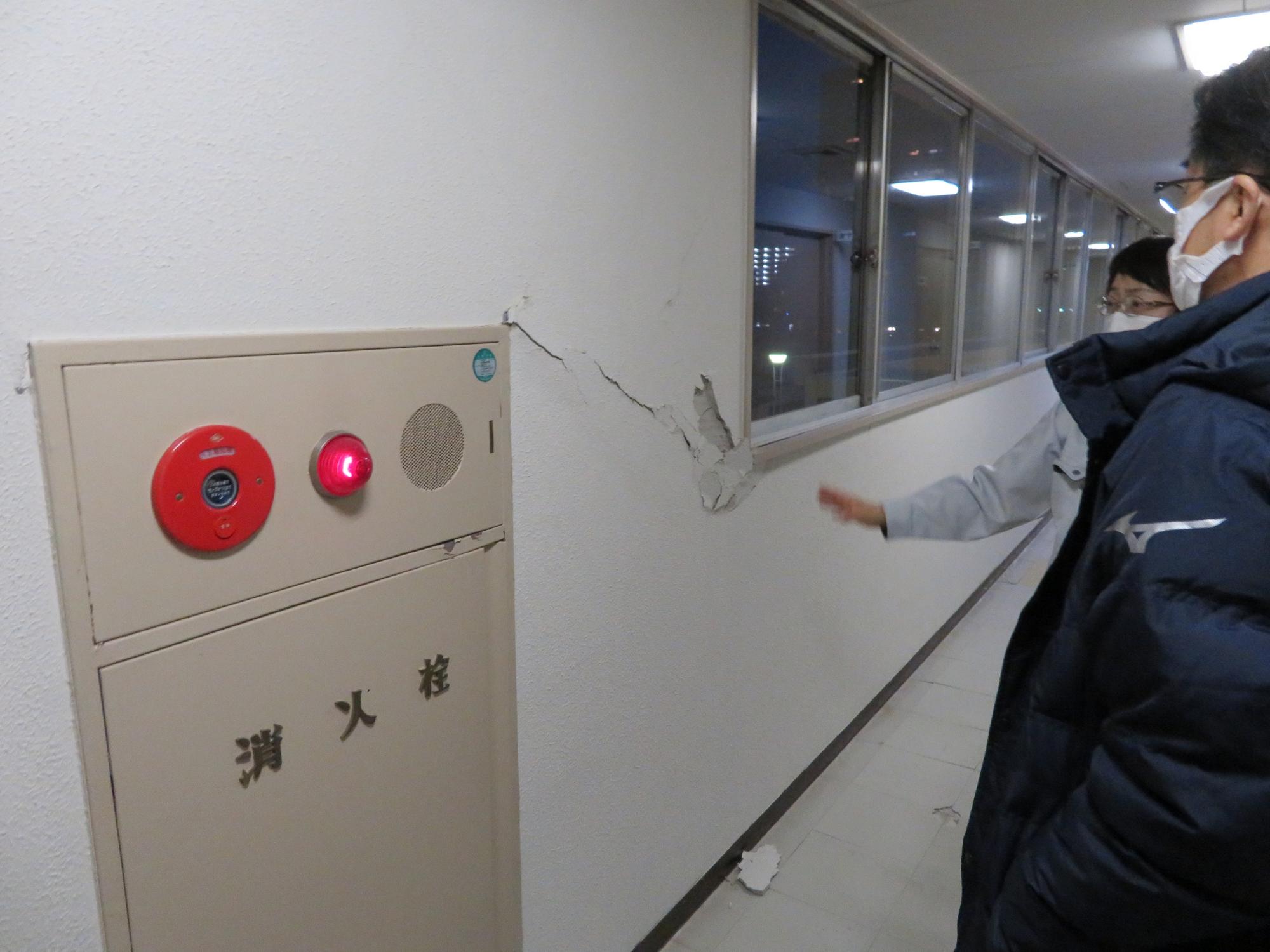 建物の室内で、消火栓横のひび割れた壁を市長と関係者が見ている写真