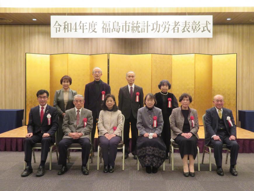 「令和4年度福島市統計功労者表彰式」のボードがある金屛風の前で、前列に市長の横に5名が座り、後列に4名が立っている写真