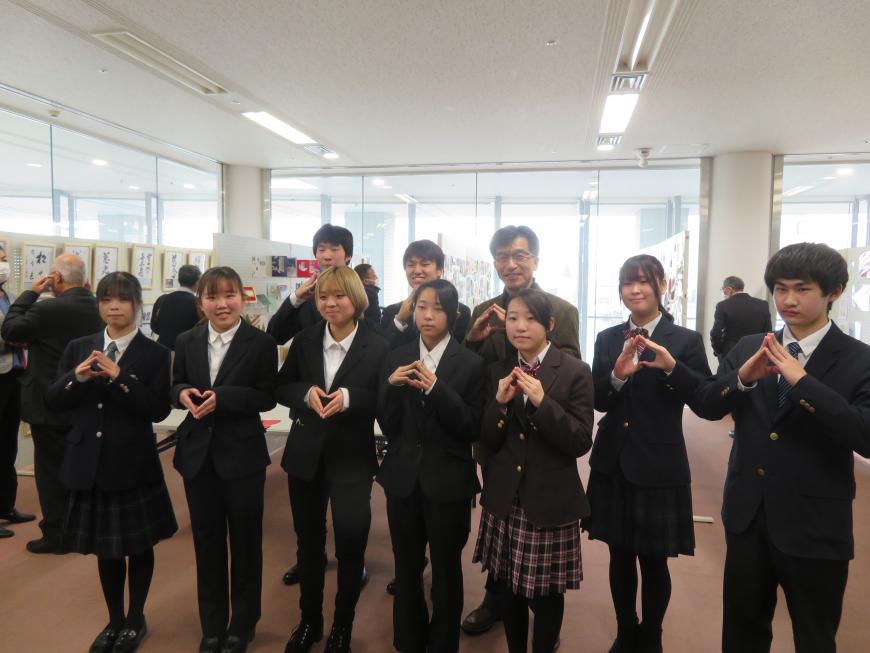 女性6名、男性3名が市長と2列になって両手の指先を合わせてポーズをとっている写真