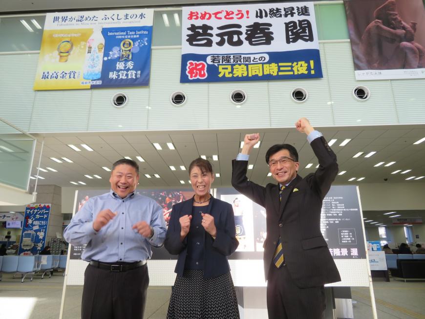 若元春の小結昇進祝いの横断幕が飾られたロビーの下で市長と男女各1名がガッツポーズをしている写真