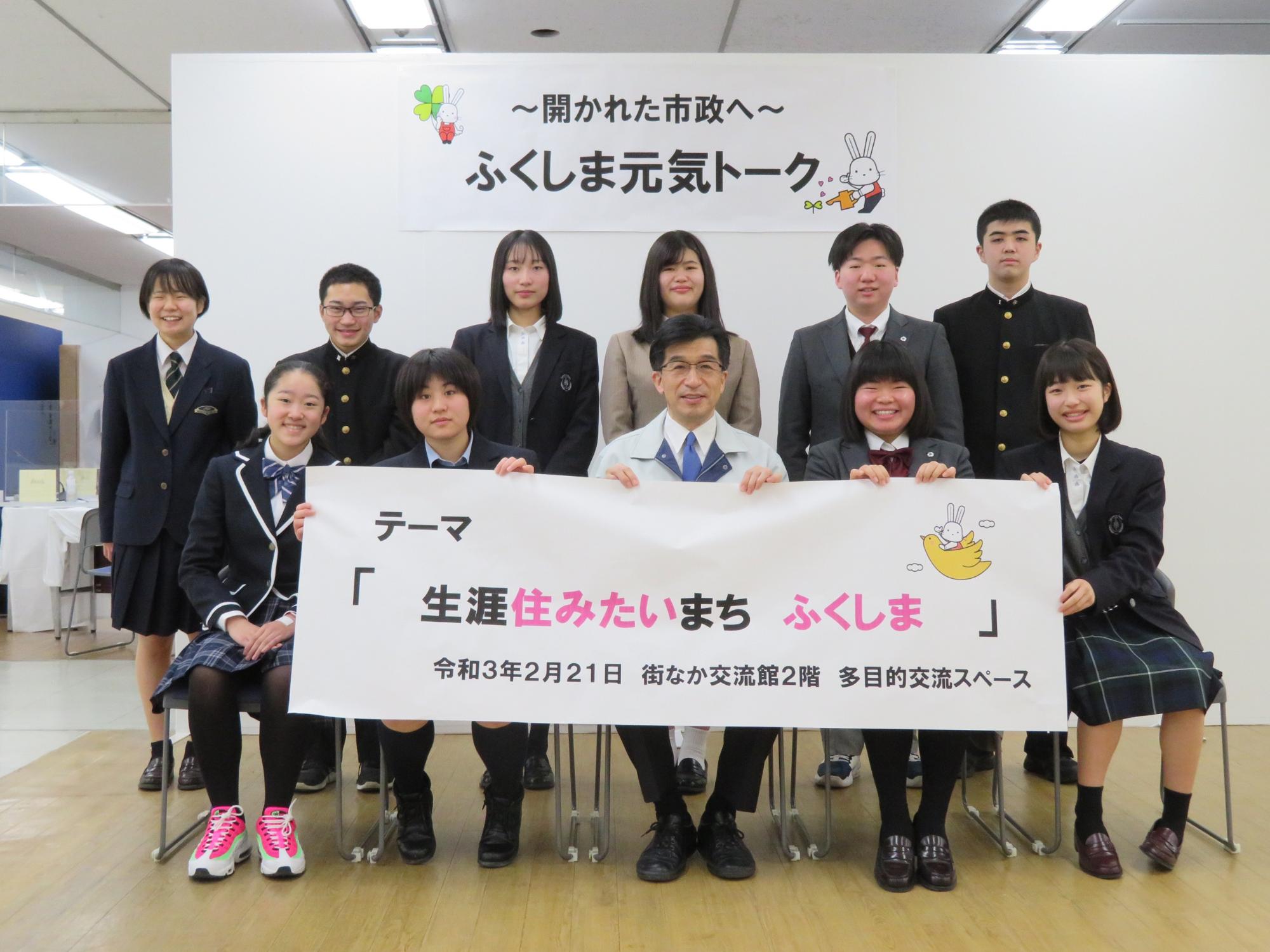 「~開かれた市政へ~ふくしま元気トーク」と書かれたパネル前で、市長と制服を着た参加者たちが「生涯住みたいまち ふくしま」と書かれた横断幕を手に持っている写真